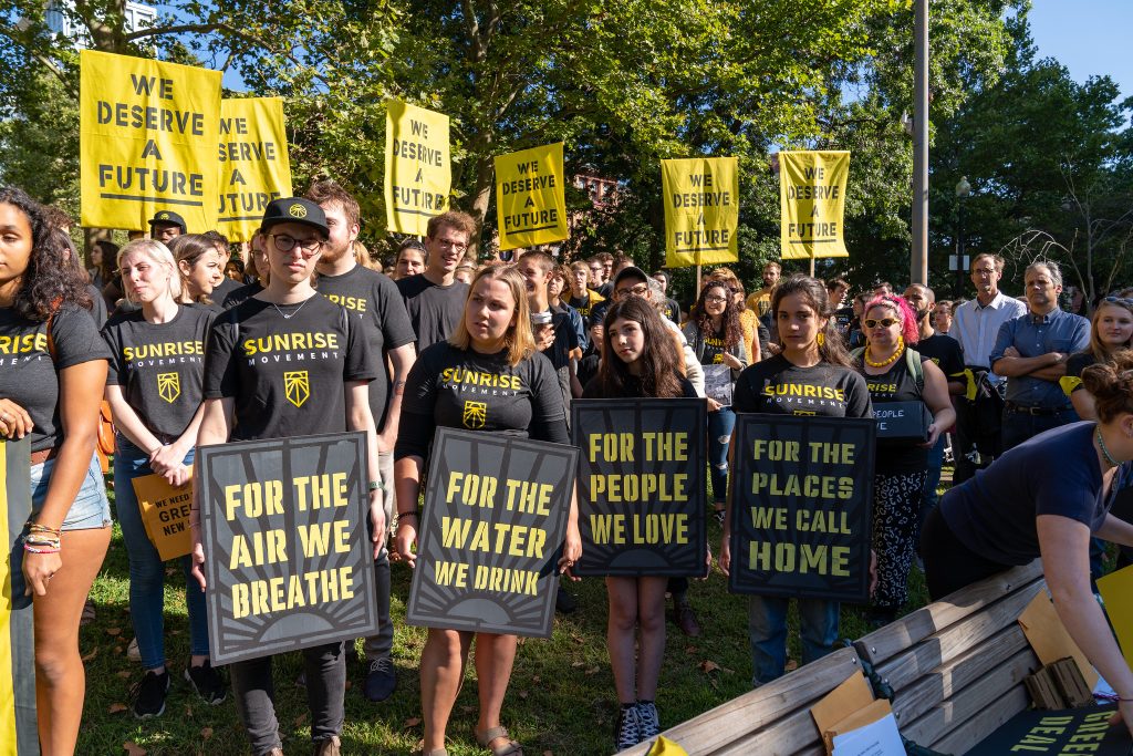 Sunrise demonstrators protest. Their signs say "for the air we breathe, for the water we drink, for the people we love, for the places we call home, we deserve a future."