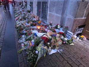A vigil for Charlie Hebdo. Flowers of all colors and candles are placed on a cobblestone sidewalk.
