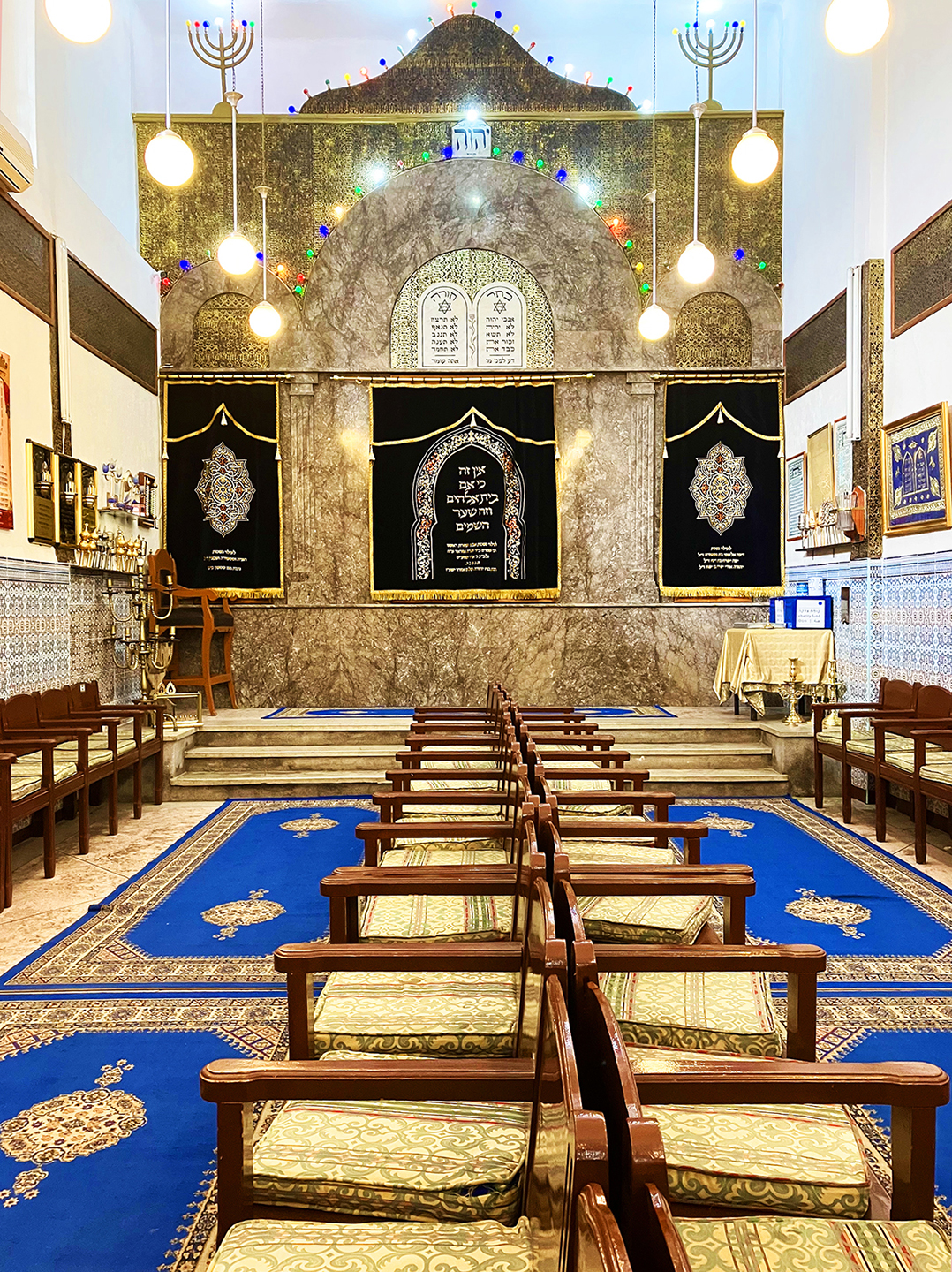 Two rows of wooden chairs stretch back-to-back from the center of the foreground towards a low platform and an ornate ark.