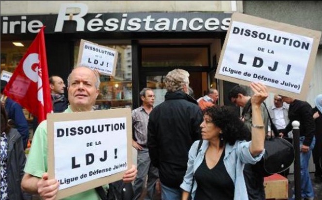 A crowd stands in front of a building caling for the dissolution of the Jewish Defense Leage