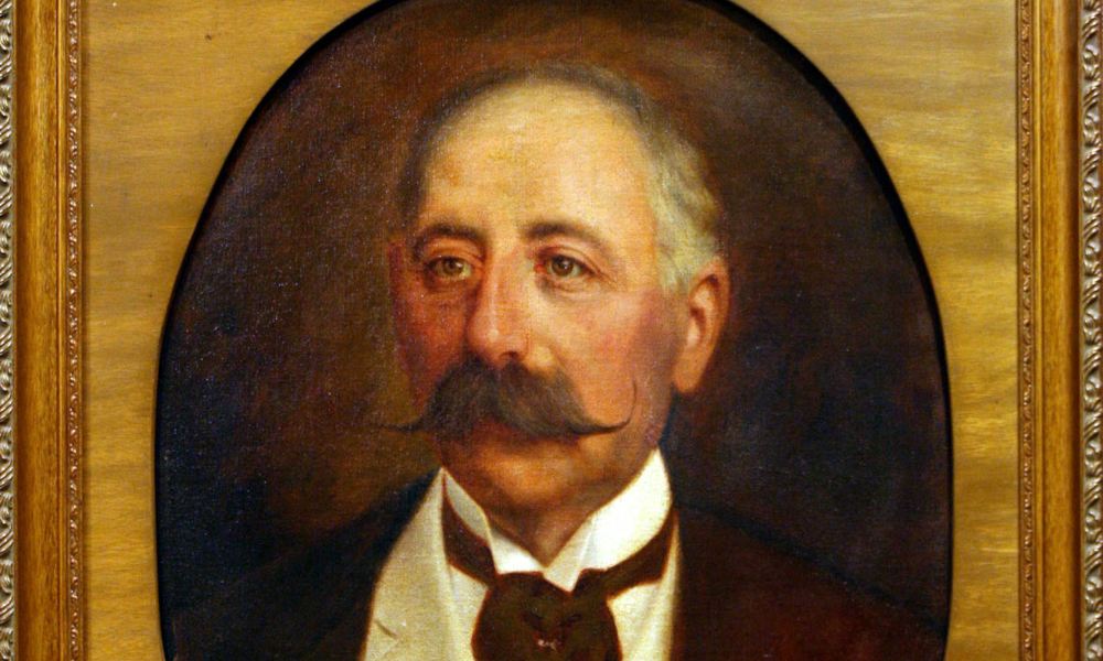 A portrait of Baron Maurice de Hirsch, a balding man with graying head hair and a magnificent mustache.