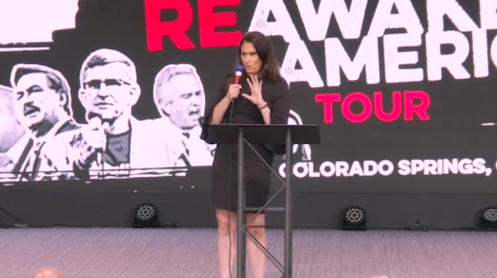 A woman in a black dress speaks into a microphone on stage