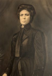 An old black and white photograph of a woman in a black wig and black clothes.