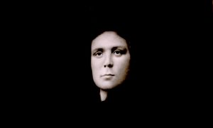 A serious woman's face is surrounded by black.