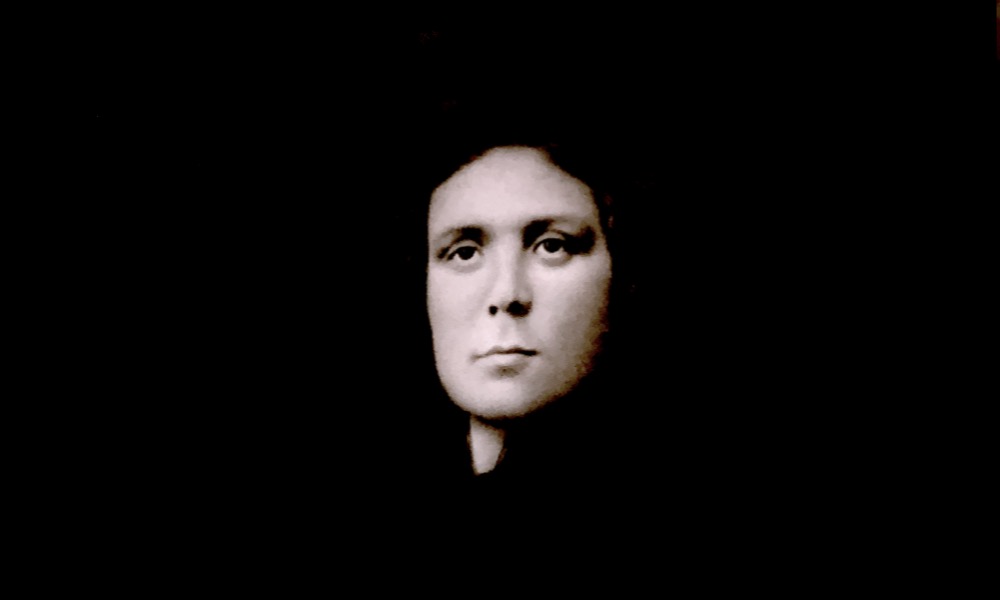 A serious woman's face is surrounded by black.