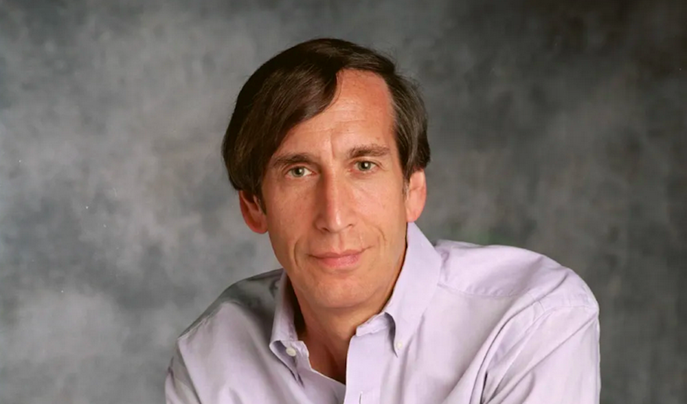 A broad-souldered white man with brown hair gazes at the camera