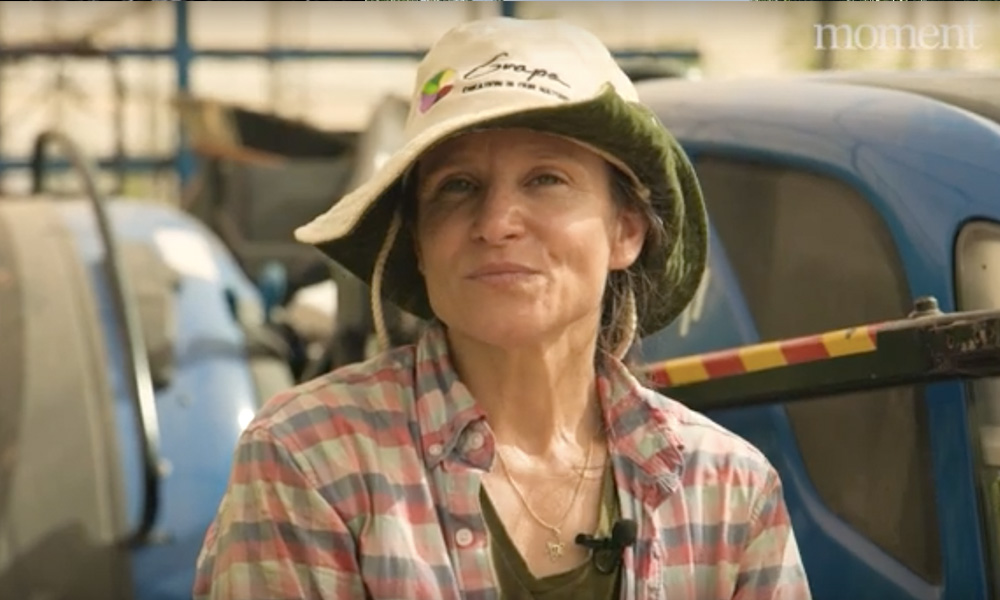 A woman in work clothes looks at the camera