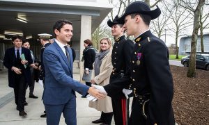 Gabriel Attal walking out of a building and shaking the hands of soldiers