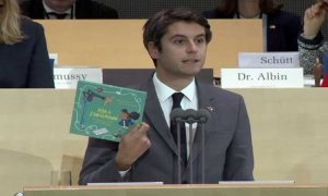 Gabriel Attal sitting in an assembly and talking while holding a book called, "Ada & Zangemann"