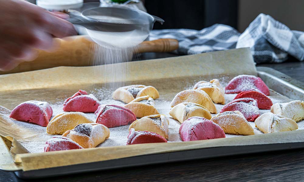 Poppy seed hamantaschen being prepared by being sprinkled with powdered sugar.