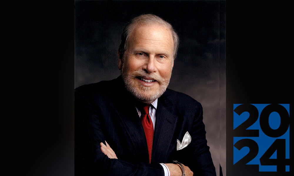 Man in a suit with a red tie with short, white hair and beard