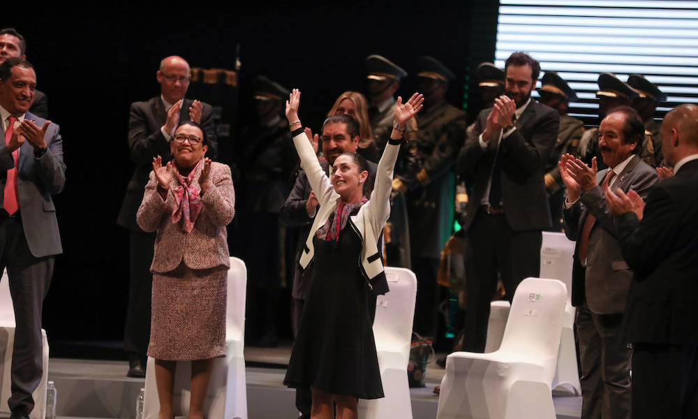 Woman stands center stage with her hands in the air while those around her applaud.