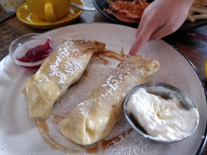 Two blintzes on a plate and a hand picking at sauce on the plate.