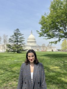 Young women in glasses and a blazer stands in front of the U.S. capitol.
