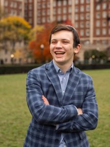 Young man wearing a kippah and blue plaid blazer smiling. 