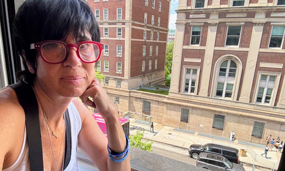 Woman in red-framed classes with short black hair sits next to a window overlooking the street