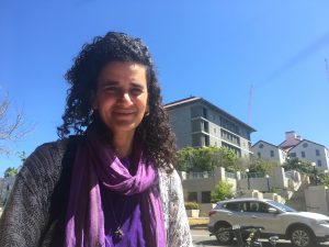 Woman with dark curly hair wearing a purple scarf.