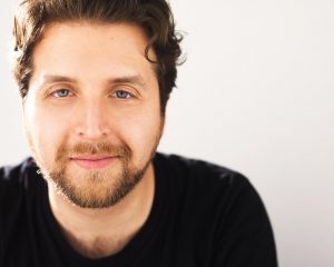 Man with a trimmed beard, blue eyes, and short brown hair.