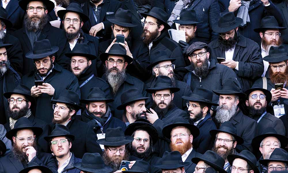 A large crowd of men standing very close together. Their faces have a variety of expreessions but all are wearing black jackets and hats.