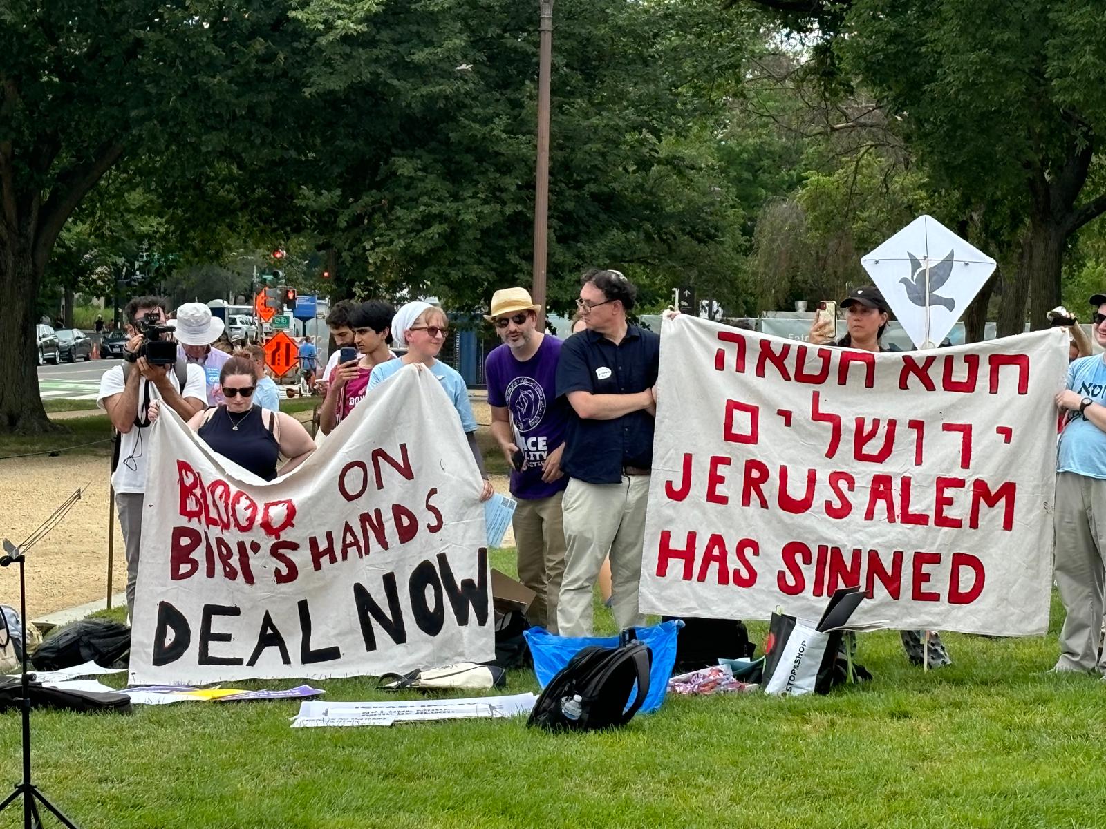 A group of people hold two large canvas banners. One says "Blood on Bibi's hands, DEAL NOW" and the other says, first in Hebrew then in English, "Jerusalem has sinned."
